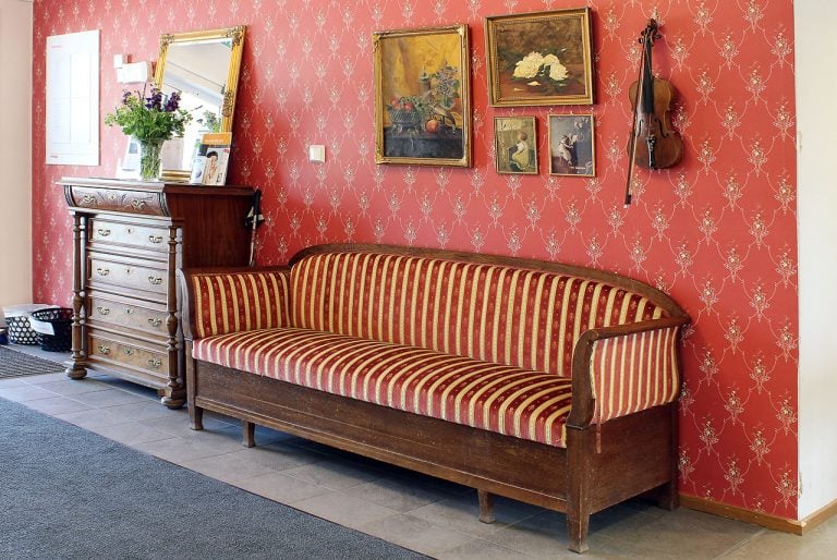 vägg med rödmönstrad tapet, byrå soffa i gammal stil, tavlor, fiol hänger på väggen