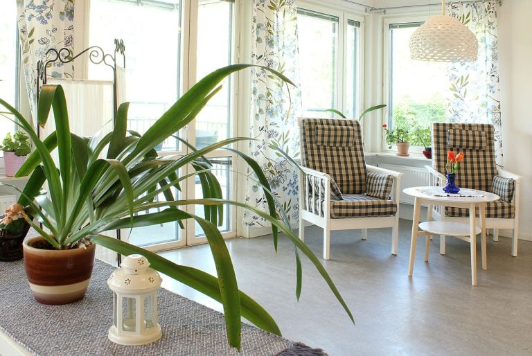 del av rum, stolar med vit/blått tyg, grön växt, balkongdörr, mönstrade gardiner