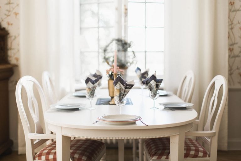 matbord med vita möbler dukat med tallrikar och vinglas med servetter