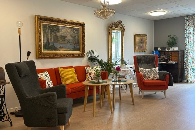 Rymlig gemensam yta med soffa, fåtöljer, soffbord och piano. Stora tavlor och helkroppsspegel på väggen, kristallkrona i taket.