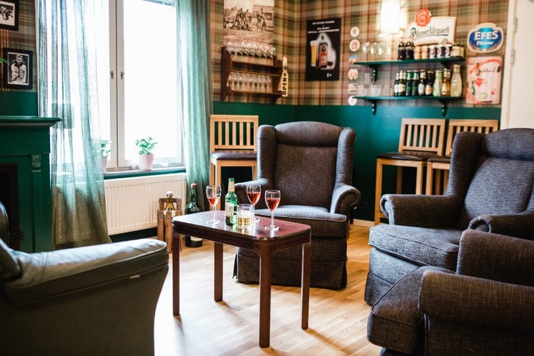 barmiljö gröna väggar, flaskor på bänk, blå fåtöljer , vinglas och ölflaska på bord