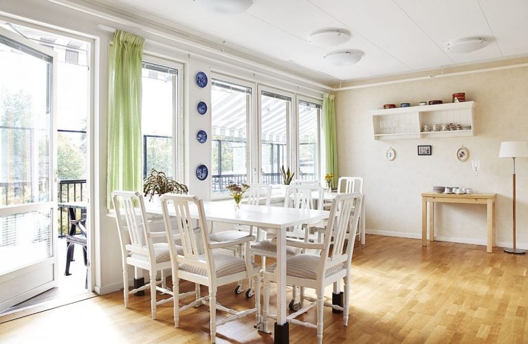 Ljust rum, vitt bord, vita stolar, gröna gardiner, balkongdörr ut