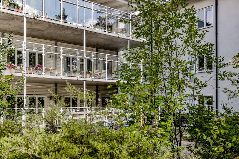 tre våningar med balkonger med genomskinliga räcken växter i förgrund