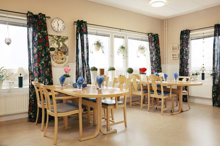 köksbord -stolar i trä glas med blå servetter på borden, svartmönstrade gardiner