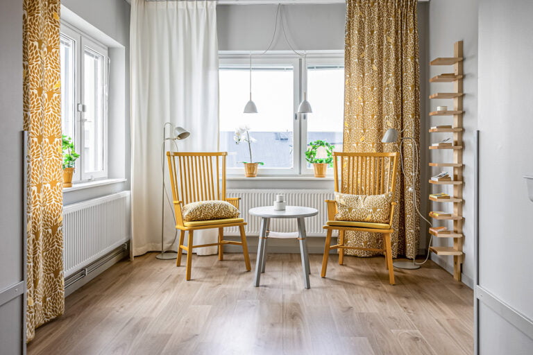 fönsterhörna med gula stolar med kuddar och gardiner i samma gula mönster litet bord