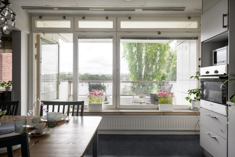 Stora fönster och öppen balkongdörr med utsikt mot vattnet. Dukat bord i förgrunden