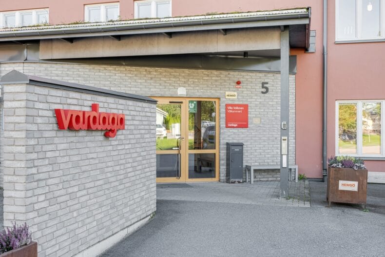 Boendets fasad i grått tegel och röda Vardaga-skyltar.
