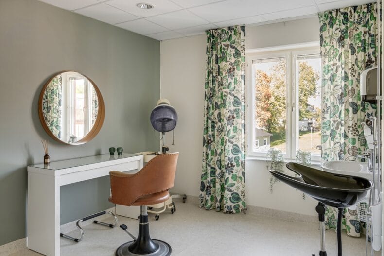 Boendets eget rum för frisering, med handfat för hårtvätt och frisörstol framför vägghängd spegel.