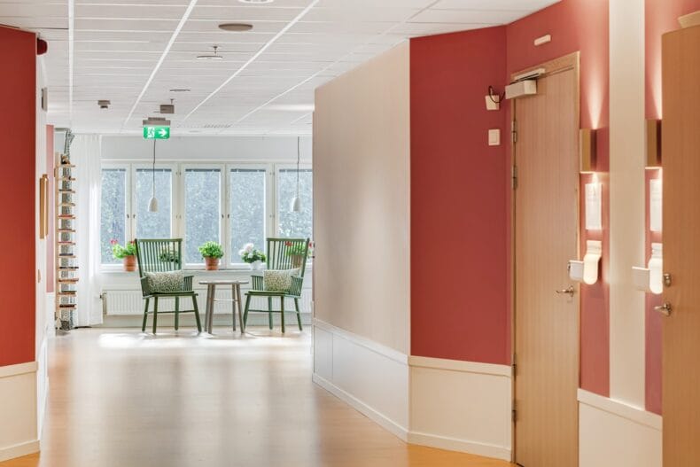 Korridor med röda väggar. I bakgrunden syns två pinnstolar vid fönstren.