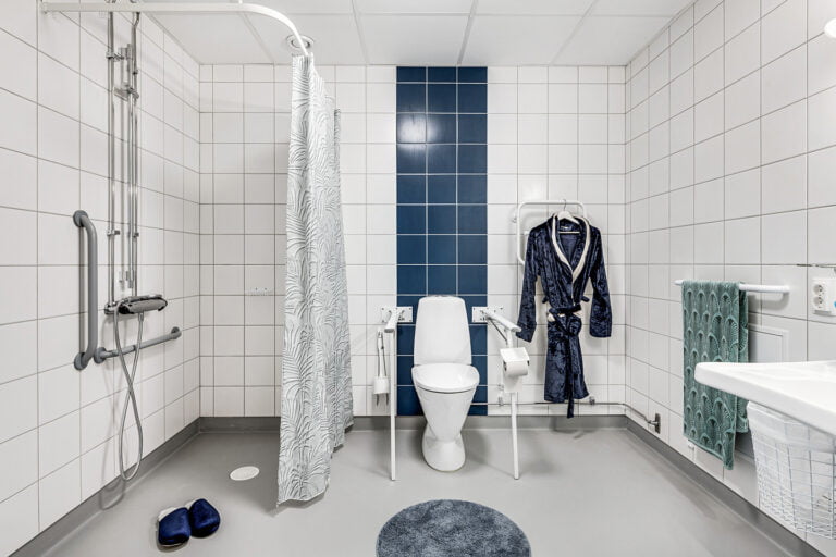 badrum duschdraperi vitt kakel men blått kakel bakom toalett blå morgonrock på galge