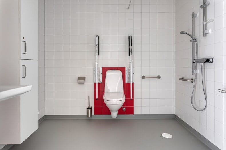 Badrum med anpassningar för rörelsehindrade vid dusch och toalettstol.