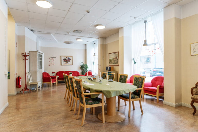 Sofiagården: gemensamt rumstort rum, röda soffgrupper samt stort bord med grön duk och stolar
