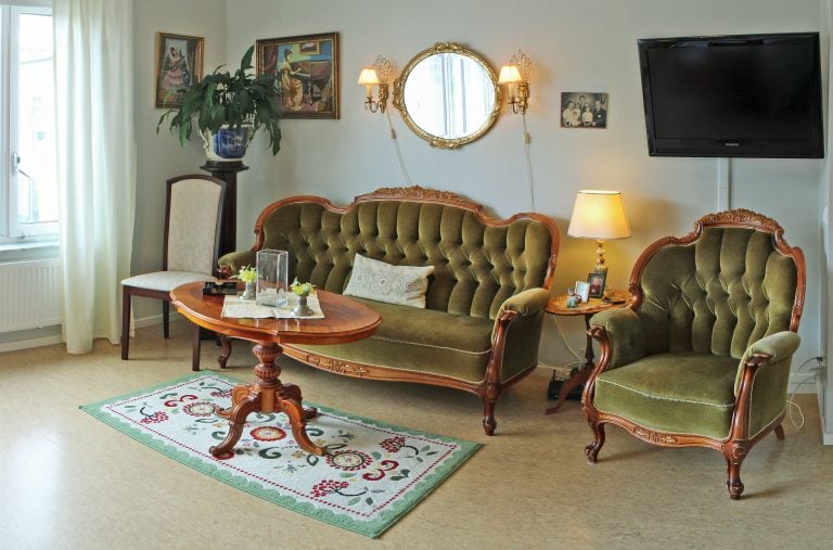 gammaldags möblering soffa stol i grön sammet ovalt bord matta spegel tv på vägg