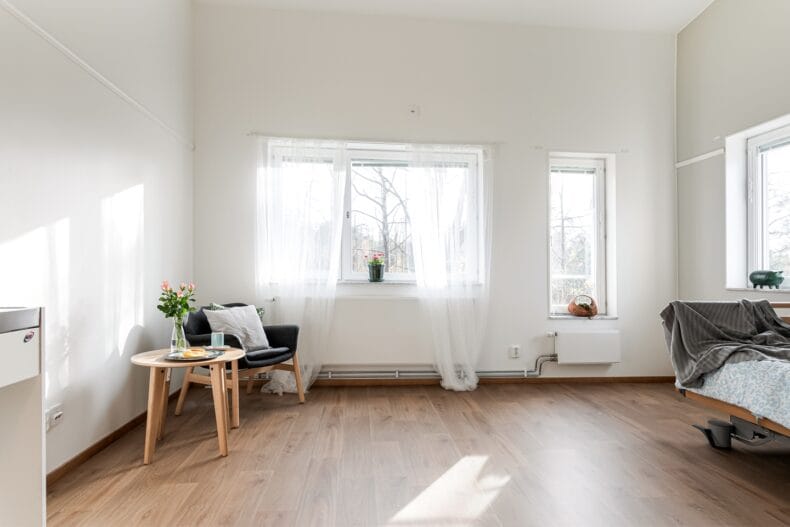 Ljust och rymligt rum med stora fönster, fåtölj och justerbar säng i lugna färger.