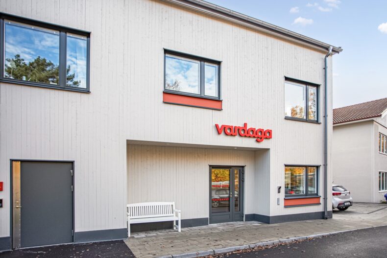 Entré med ljus fasad och röd Vardaga-logotyp ovanför dörren.