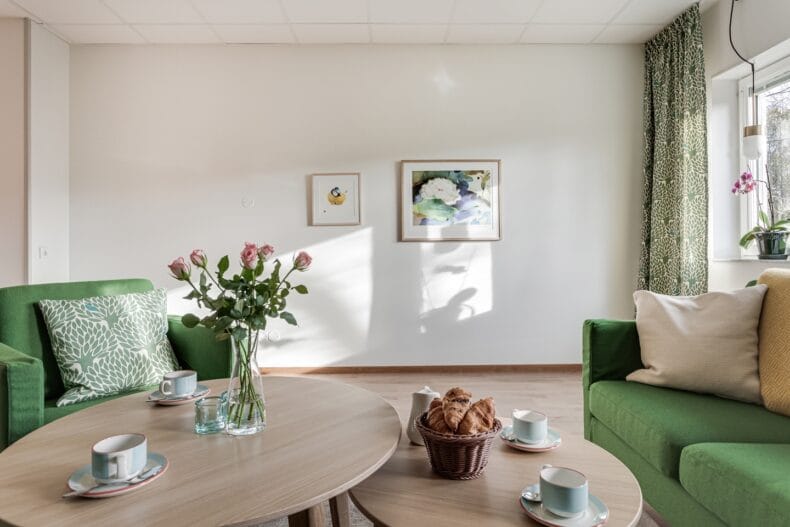 Närbild på vardagsrumsbord med kaffekoppar, rosor i vas och korg med croissanter.