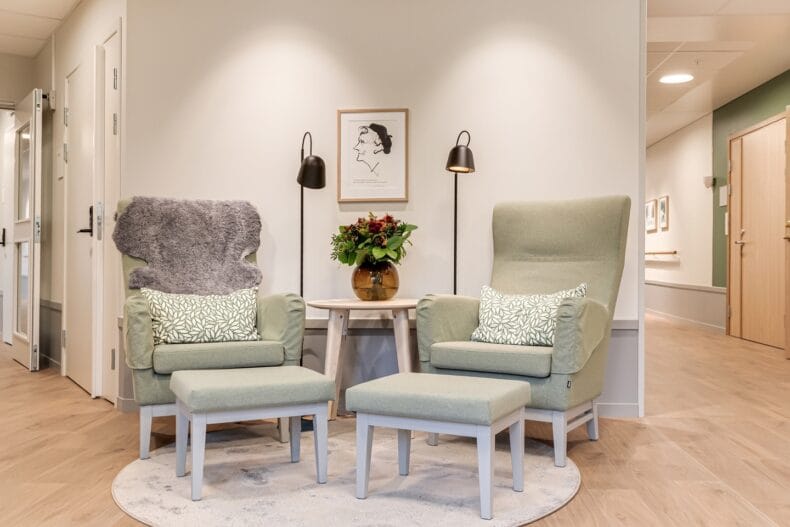 Två fåtöljer med fotpallar placerade i ett lugnt hörn med tavla på väggen.