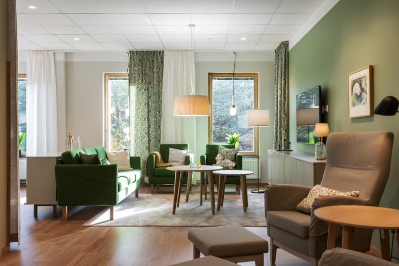 Vardagsrum i grönt tema. Inbjudande vardagsrum med gröna soffor och fåtöljer, stora fönster och ljus inredning med naturkänsla.