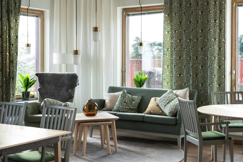 Närbild av vardagsrum i grönt tema. Del av vardagsrum med grön soffa, mönstrade gardiner och kuddar.