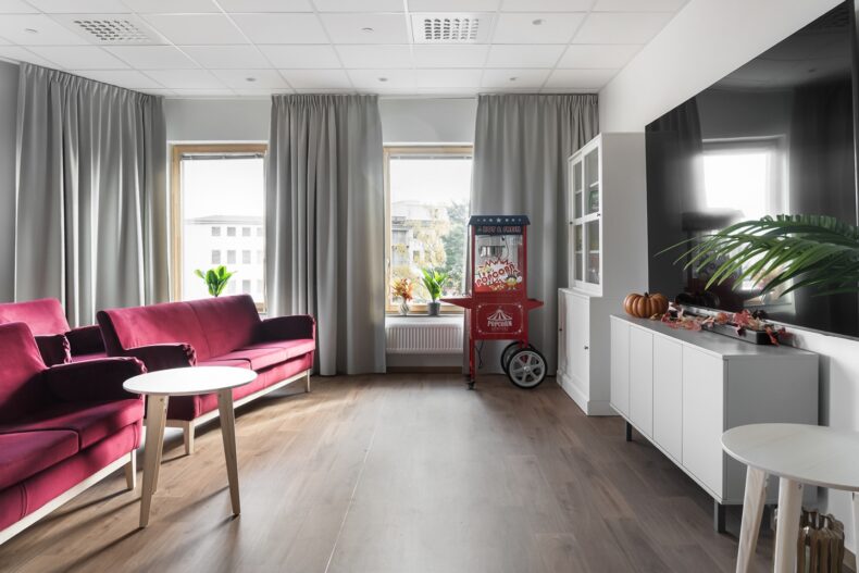 Aktivitetsrum med biosoffor. Ljust rum med röda soffor, stor tv och en röd popcornvagn, dekorerat.