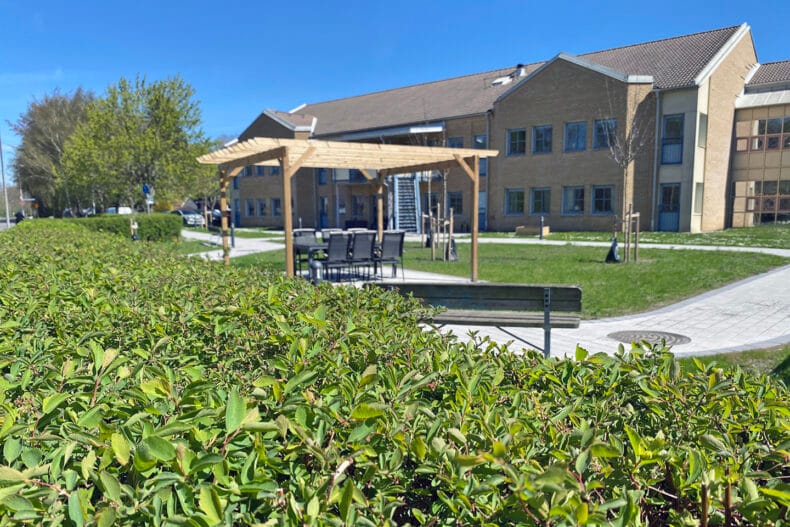 Fasad ljusbrun tegel byggnad med gröna växter i förgrunden