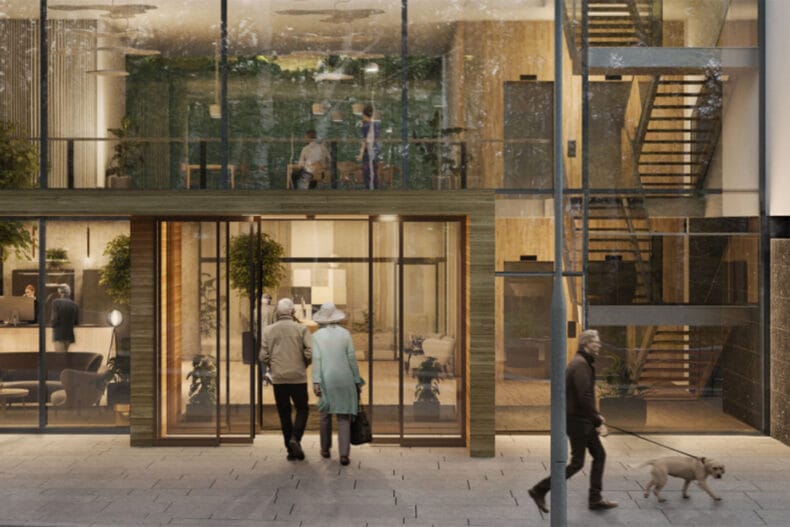 Entrén sedd utifrån, stora glasfönster, två äldre personer går in genom automatiska skjutdörrar