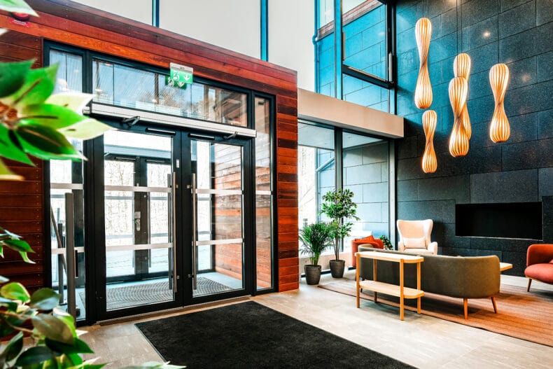 Entrén med stora glaspartier, dörrar med svart ram, svart lång dörrmatta på trägolv