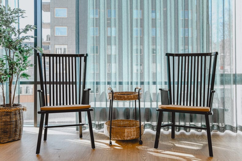 Två svarta karmstolar placerade mot stora fönster, grön skir gardin