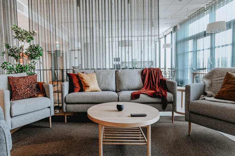 Sällskapsrum med grå soffgrupp, runt bord i ek, röd orange kuddar och filt