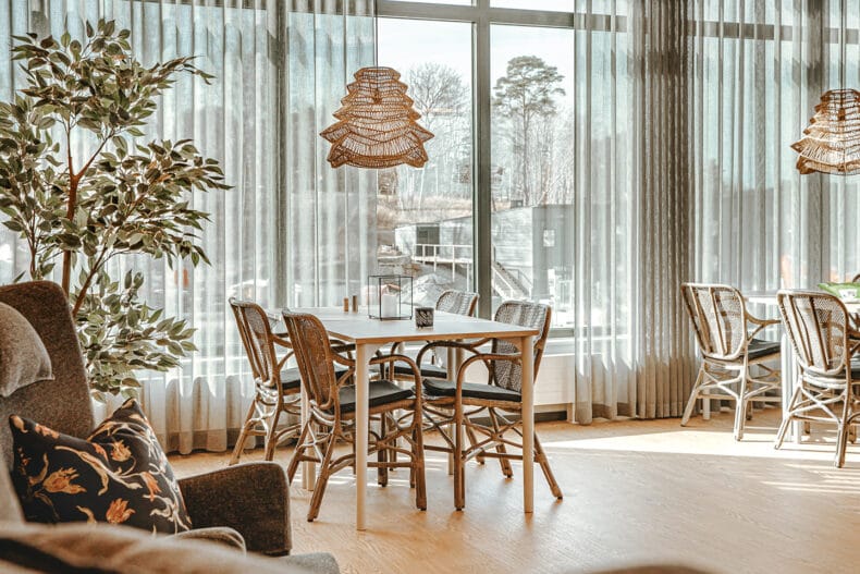 Sällskapsrum med ekbord och rottingstolar, skira gardiner och stora fönster